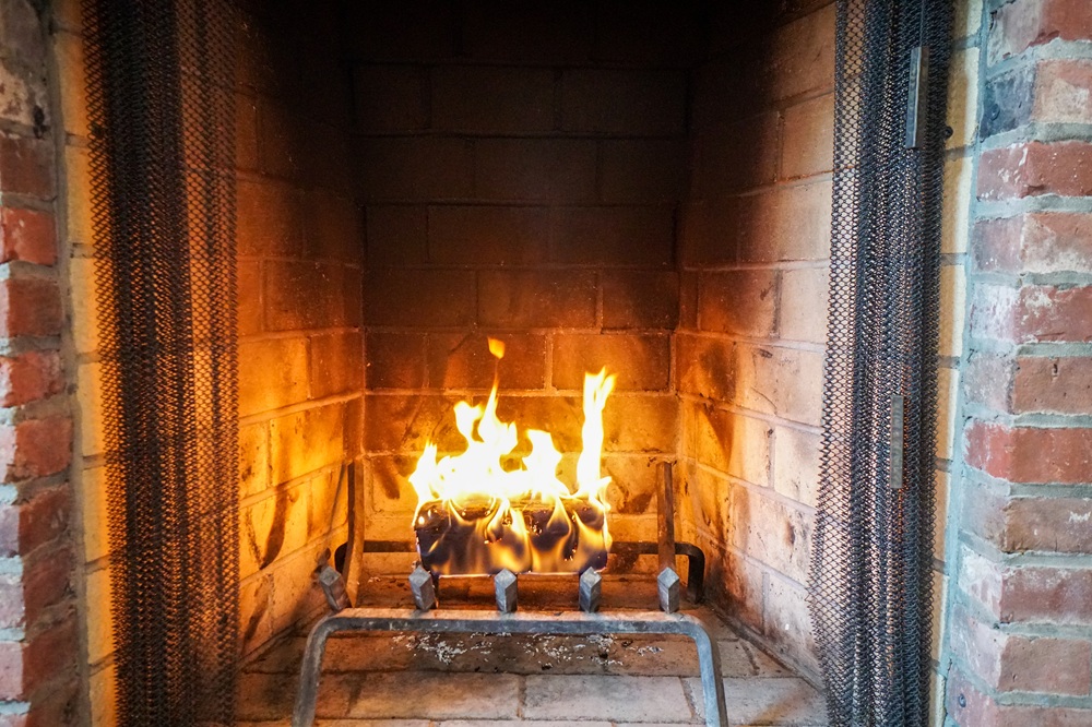 Burning logs in a brick fireplace with protective chain mesh screen