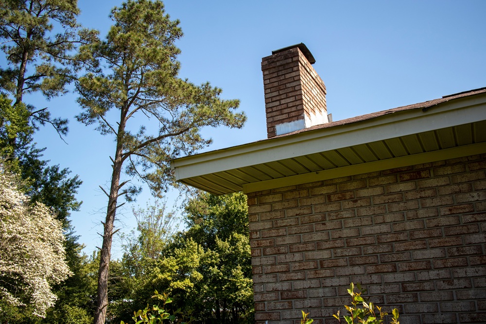 Brick home exterior with chimney visible above the roofline on a sunny day