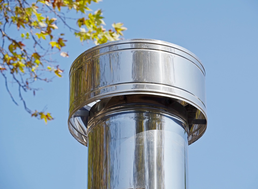 Shiny stainless steel chimney cap against a blue sky with autumn leaves — chimney service