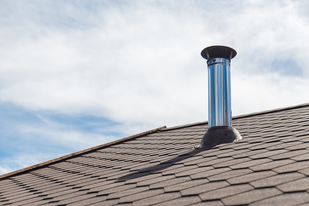 Metal chimney liner pipe installed on a residential rooftop under a partly cloudy sky
